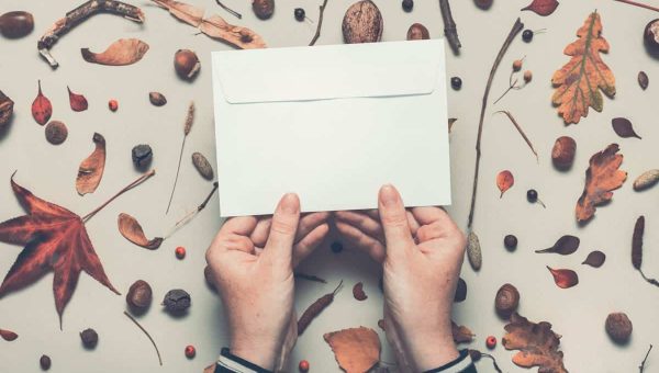 Woman holding blank post mail envelope mock up with autumn arrangement flat lay top view copy space